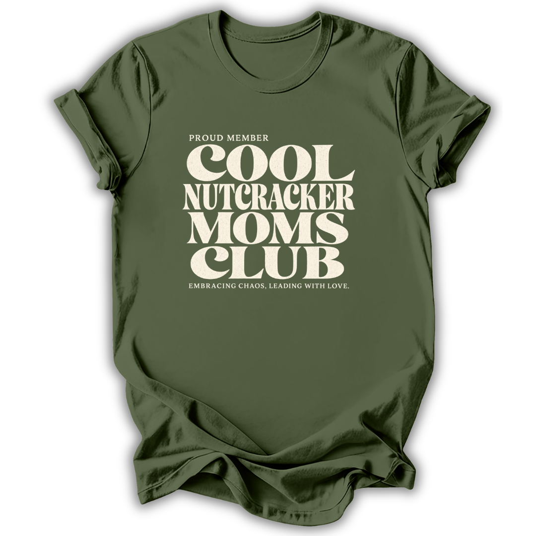 Green short-sleeve crewneck t-shirt with a cream-colored retro graphic that reads 'PROUD MEMBER COOL NUTCRACKER MOMS CLUB' and 'EMBRACING CHANGE, LEADING WITH LOVE.'.
