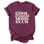 A maroon short-sleeve crewneck t-shirt with a cream-colored retro graphic that reads 'PROUD MEMBER COOL NUTCRACKER MOMS CLUB' and 'EMBRACING CHANGE, LEADING WITH LOVE.'.