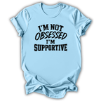 A light blue short-sleeve t-shirt with the text 'I'M NOT OBSESSED I'M SUPPORTIVE' printed in black across the chest, shown on a plain white background.