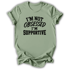 A sage green short-sleeve t-shirt with black text on the front reading 'I'M NOT OBSESSED I'M SUPPORTIVE', displayed against a clean white background.