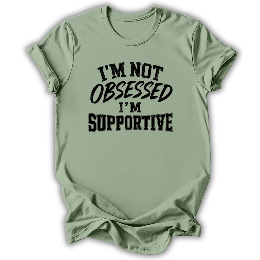 A sage green short-sleeve t-shirt with black text on the front reading 'I'M NOT OBSESSED I'M SUPPORTIVE', displayed against a clean white background.