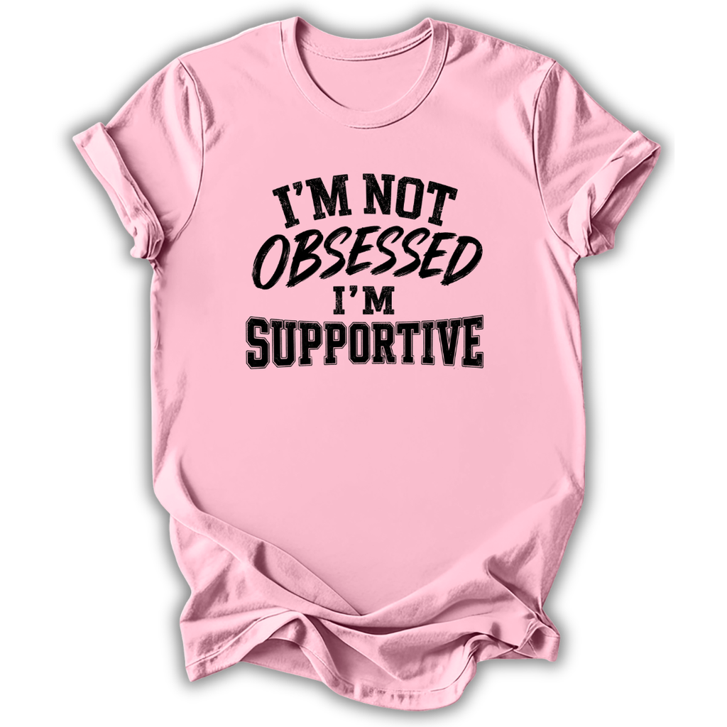 A light pink short-sleeve crewneck t-shirt with the text 'I'M NOT OBSESSED I'M SUPPORTIVE' printed in black across the chest, shown on a white background with a drop shadow.