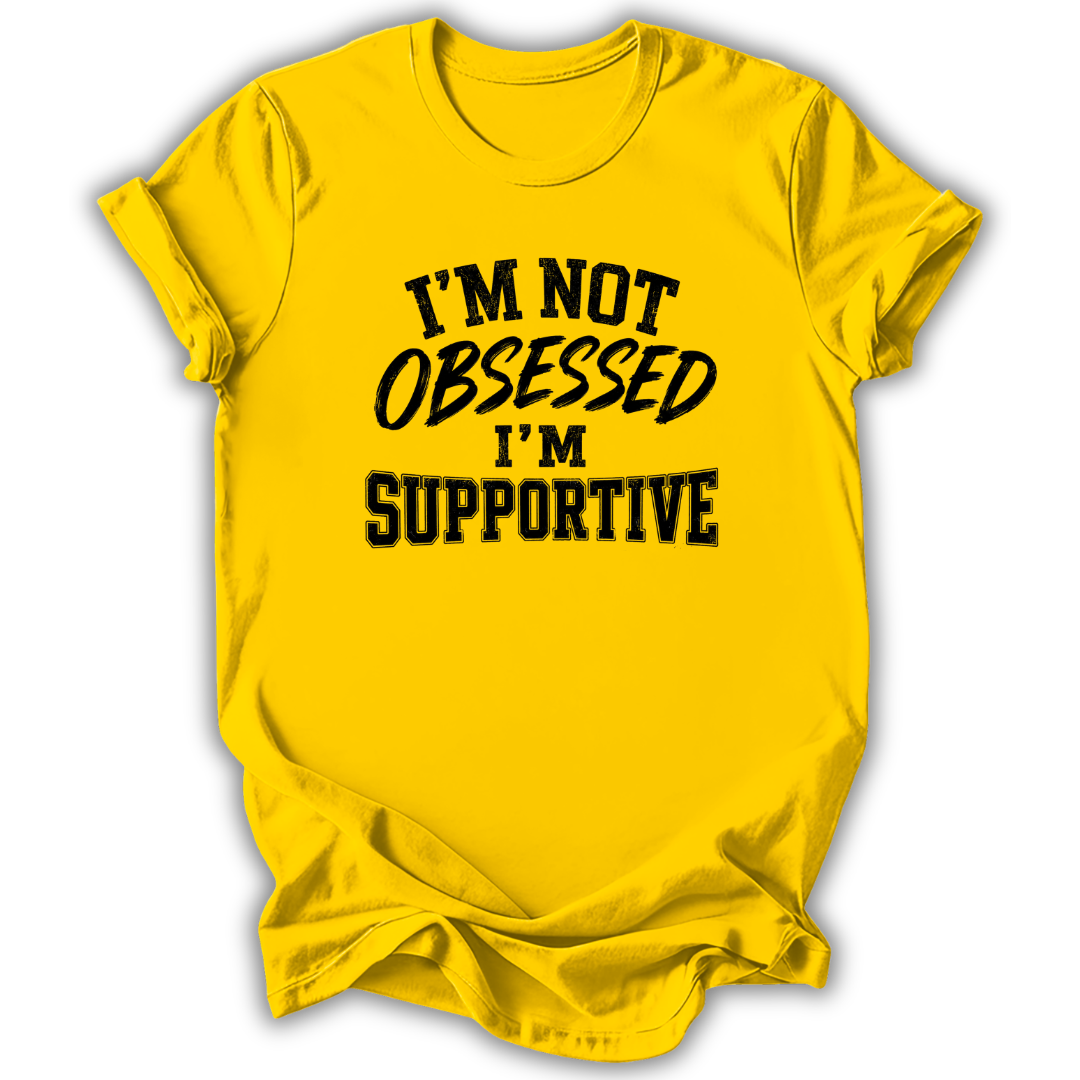 A bright yellow short-sleeve t-shirt with black text on the front reading 'I'M NOT OBSESSED I'M SUPPORTIVE' in a brush-style font, shown on a white background with a soft drop shadow.
