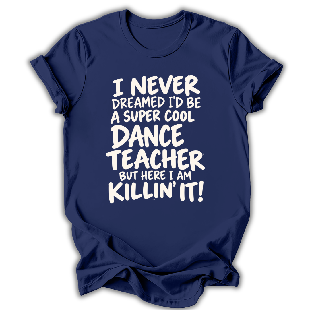 A navy blue short-sleeve t-shirt with a white graphic text print on the front that reads 'I NEVER DREAMED I'D BE A SUPER COOL DANCE TEACHER BUT HERE I AM KILLIN' IT!' on a white background.