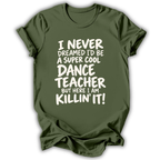 An olive green short-sleeve t-shirt with white text that reads 'I NEVER DREAMED I'D BE A SUPER COOL DANCE TEACHER BUT HERE I AM KILLIN' IT!' displayed on a clean white background.