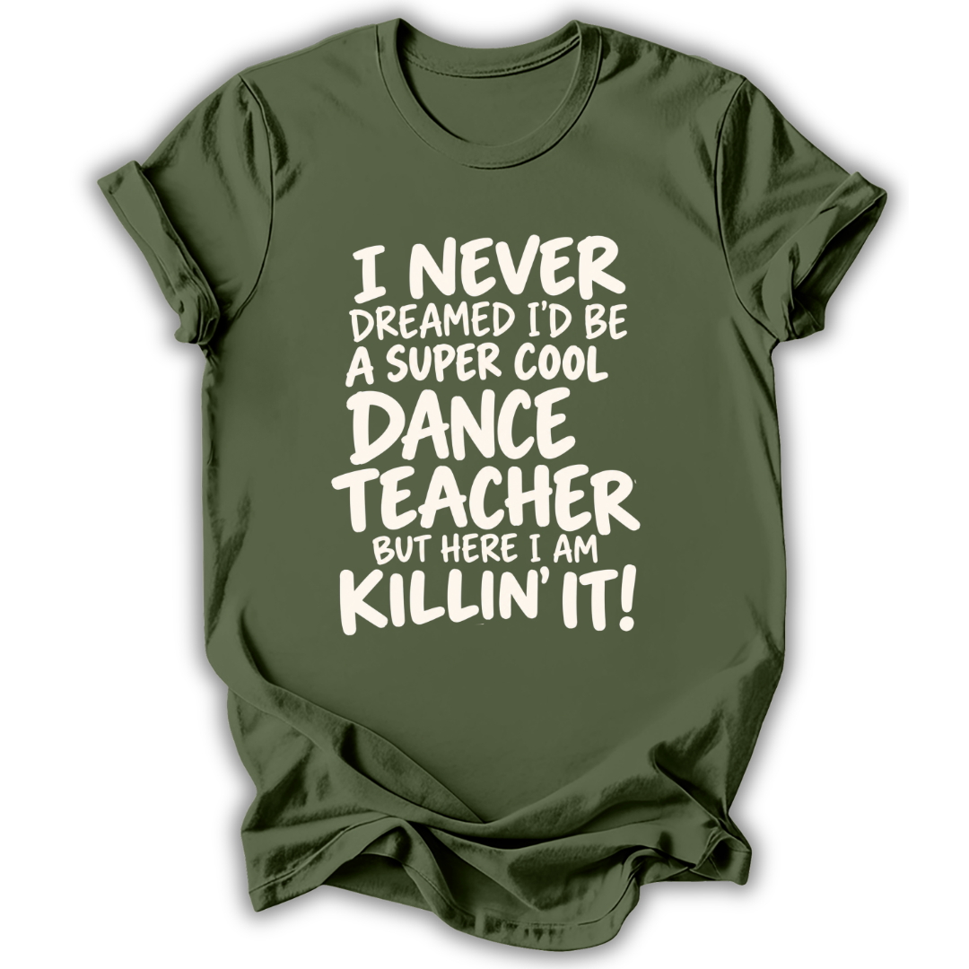 An olive green short-sleeve t-shirt with white text that reads 'I NEVER DREAMED I'D BE A SUPER COOL DANCE TEACHER BUT HERE I AM KILLIN' IT!' displayed on a clean white background.