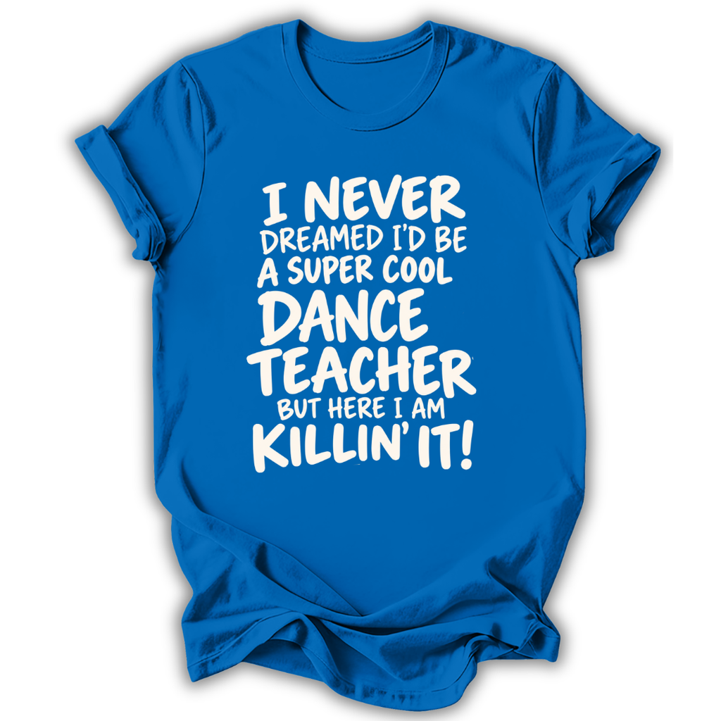 A bright blue short-sleeve t-shirt with white text that reads 'I NEVER DREAMED I'D BE A SUPER COOL DANCE TEACHER BUT HERE I AM KILLIN' IT!' displayed on a clean white background.