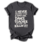 A dark charcoal gray t-shirt with a white graphic text print that reads 'I NEVER DREAMED I'D BE A SUPER COOL DANCE TEACHER BUT HERE I AM KILLIN' IT!' displayed on a clean white background.