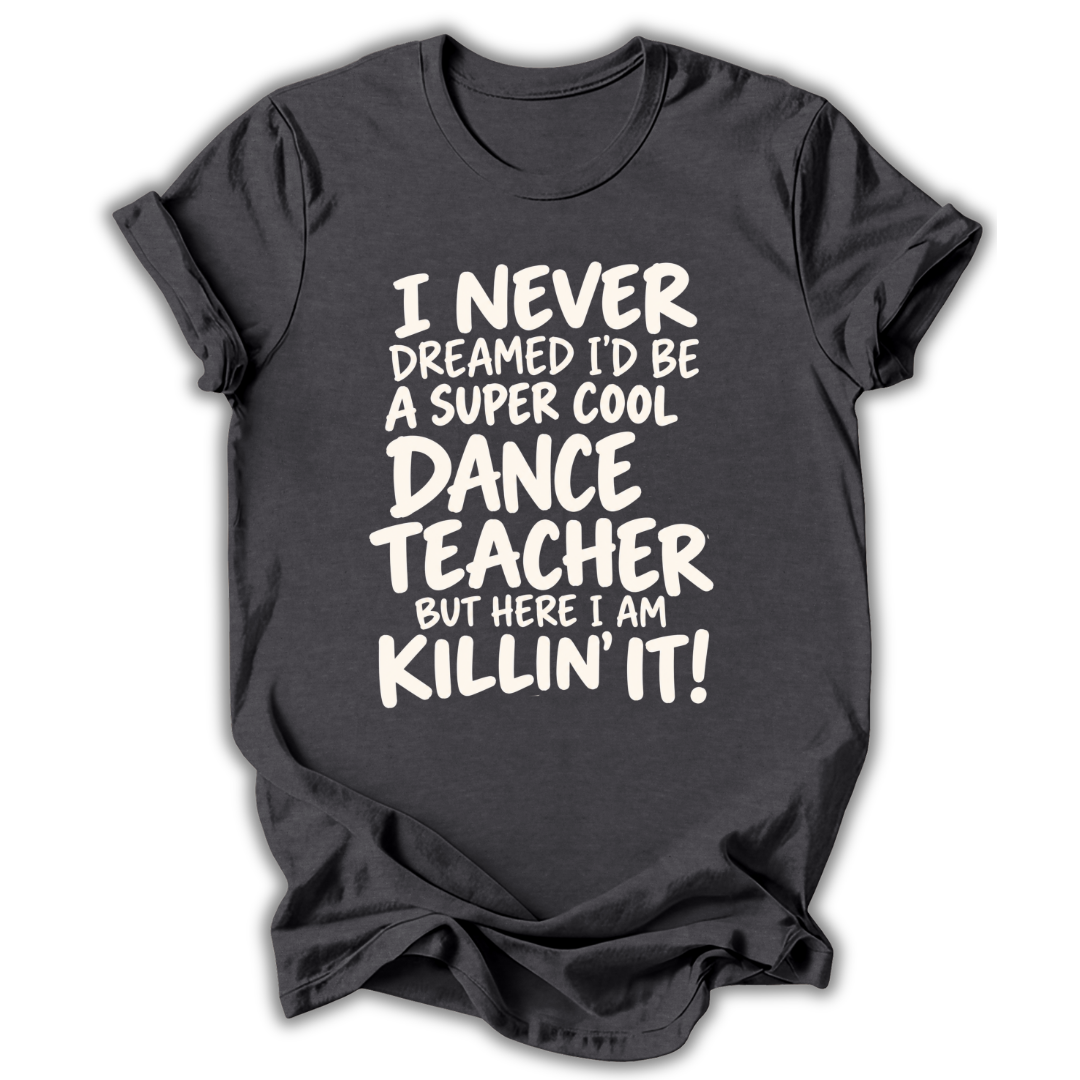 A dark charcoal gray t-shirt with a white graphic text print that reads 'I NEVER DREAMED I'D BE A SUPER COOL DANCE TEACHER BUT HERE I AM KILLIN' IT!' displayed on a clean white background.