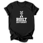 A black short-sleeve crewneck t-shirt with a white graphic print on the front showing a pair of ballet pointe shoes and the text 'BUILT DIFFERENT'.
