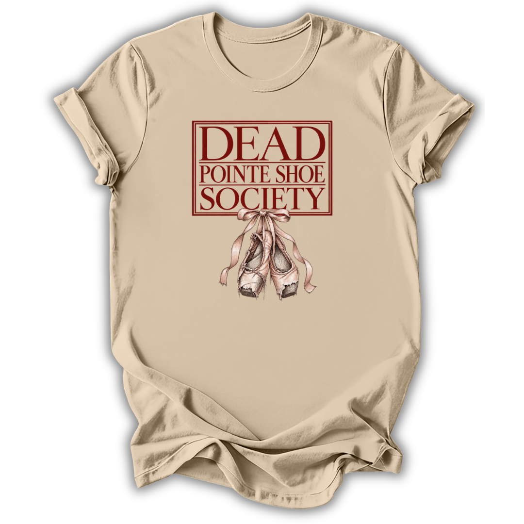 A beige short-sleeve t-shirt with a graphic print on the front reading 'DEAD POINTE SHOE SOCIETY' in dark red, above an illustration of pinkish-beige pointe shoes tied together, shown on a white background.