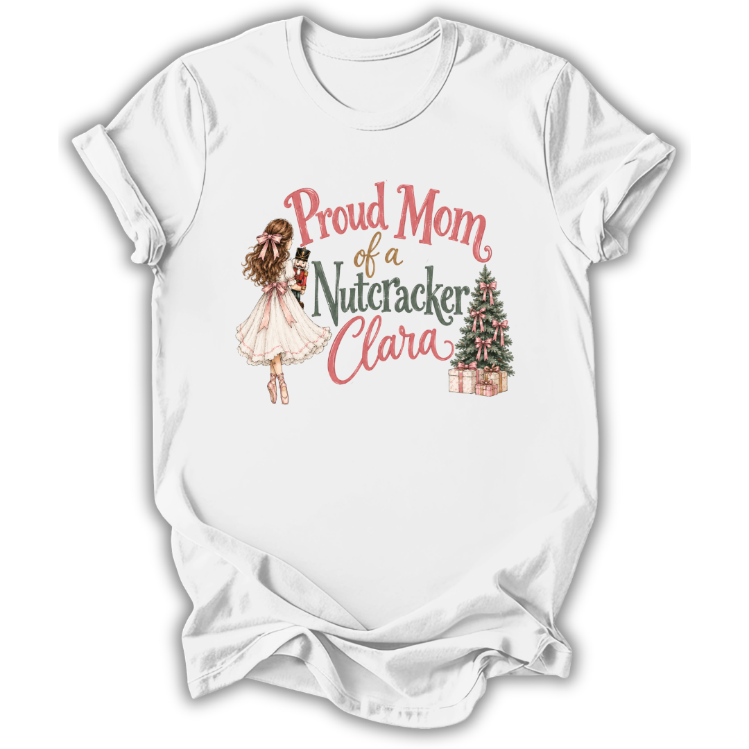 A white short-sleeve crewneck t-shirt with a graphic print on the front. The graphic features a watercolor illustration of a ballerina in a pink tutu holding a nutcracker, next to the text 'Proud Mom of a Nutacker Clara' in pink and dark green lettering, and a small decorated Christmas tree with presents.