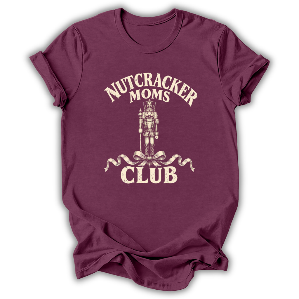 A maroon short-sleeve t-shirt with a cream-colored graphic on the front that reads 'NUTCRACKER MOMS CLUB' around a nutcracker illustration, shown on a plain white background.