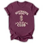 A maroon short-sleeve t-shirt with a cream-colored graphic on the front that reads 'NUTCRACKER MOMS CLUB' around a nutcracker illustration, shown on a plain white background.