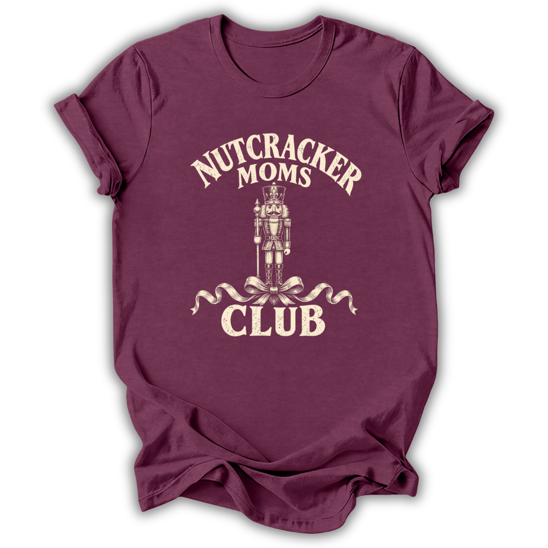 A maroon short-sleeve t-shirt with a cream-colored graphic on the front that reads 'NUTCRACKER MOMS CLUB' around a nutcracker illustration, shown on a plain white background.