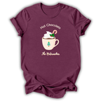 A maroon short-sleeve t-shirt with a holiday graphic on the front. The graphic shows a mug filled with hot chocolate and whipped cream, decorated with a candy cane and green sprig, with the text 'Hot Chocolate' above and 'The Nutacker' below.