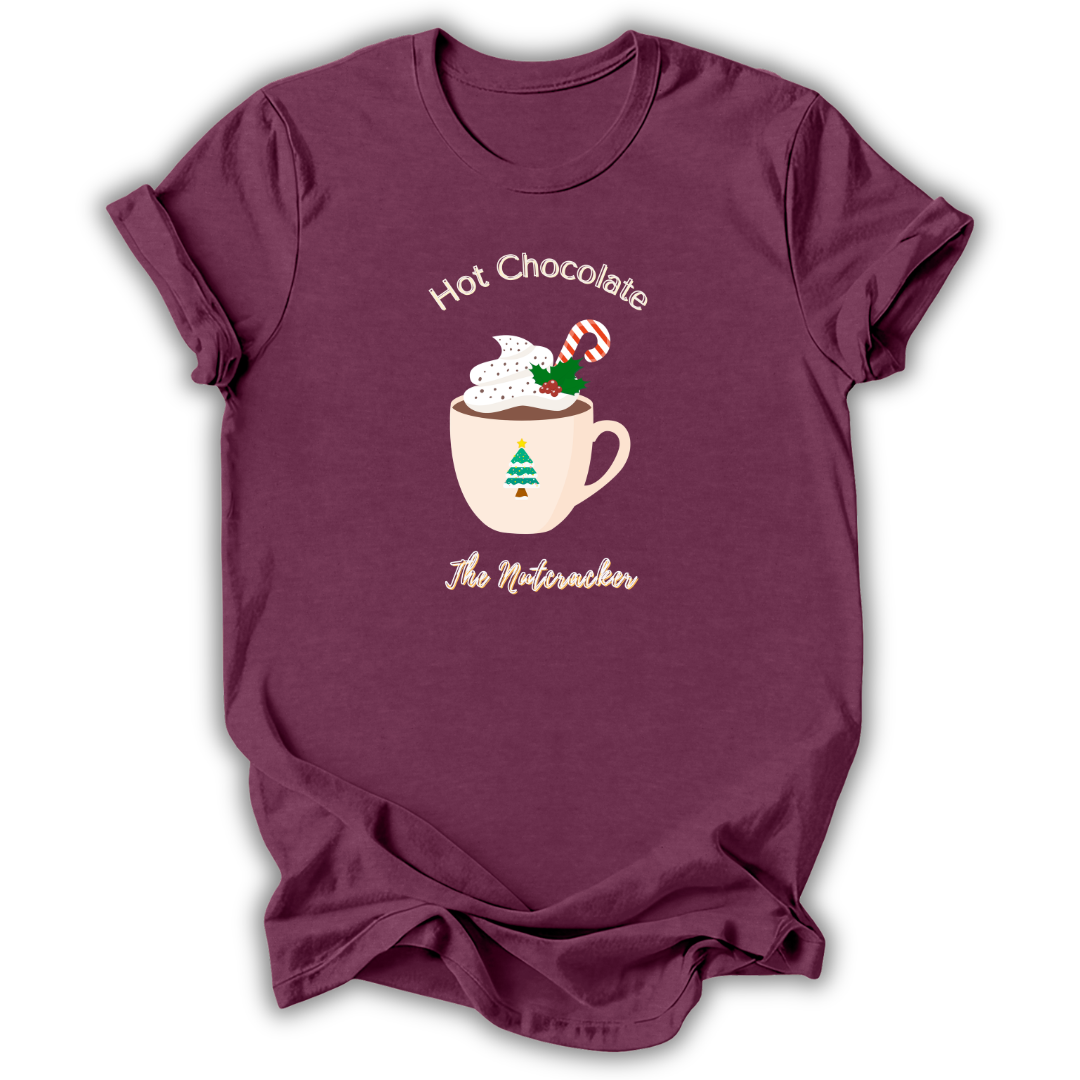A maroon short-sleeve t-shirt with a holiday graphic on the front. The graphic shows a mug filled with hot chocolate and whipped cream, decorated with a candy cane and green sprig, with the text 'Hot Chocolate' above and 'The Nutacker' below.