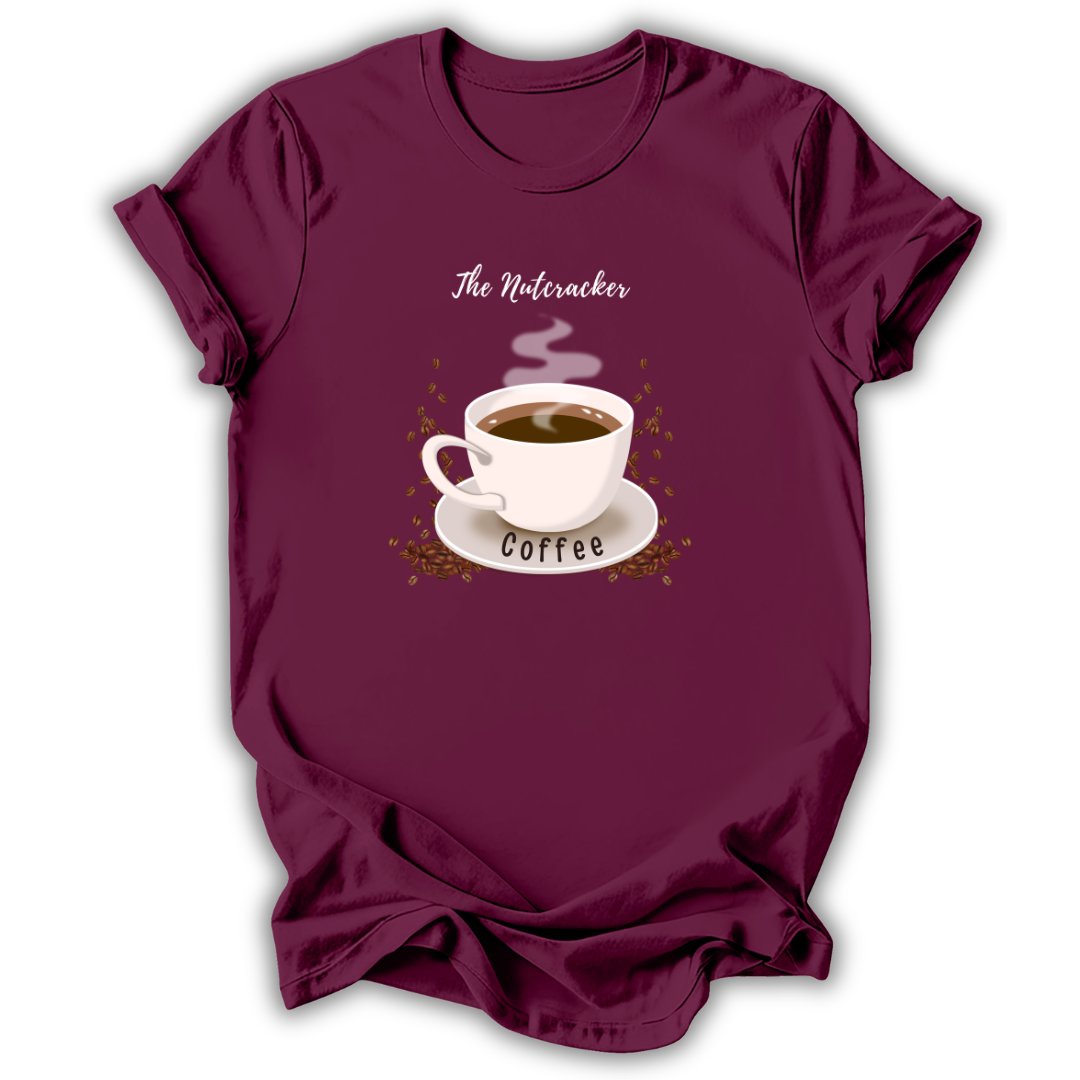 A maroon short-sleeve t-shirt with a graphic print of a steaming coffee cup on a saucer, surrounded by coffee beans, with the text 'The Nutcracker' above and 'Coffee' below, displayed on a white background.