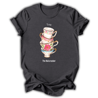 A dark charcoal gray short-sleeve t-shirt with a graphic of a stack of four floral teacups. The top cup is white with pink flowers and the word 'Tea' above it, the next is pink with gold trim, the next is light blue with a pink flower, and the bottom cup is white with gold trim and the text 'The Nutcracker' below.