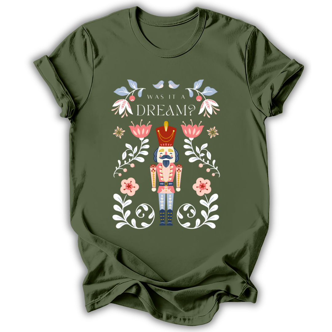 An olive green short-sleeve t-shirt with a colorful graphic of a nutcracker surrounded by flowers and the text 'WAS IT A DREAM?'.
