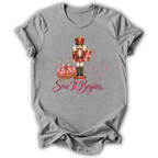 A heather gray short-sleeve t-shirt with a graphic of a nutcracker, a pink pumpkin, and the text 'Sew It Begins.