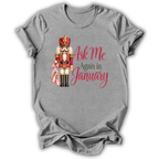 A heather gray short-sleeve t-shirt with a graphic of a nutcracker holding a pink bow and the text 'Ask Me Again in January' in pink and brown lettering.