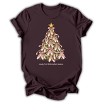 A dark plum-colored short-sleeve t-shirt with a graphic of a Christmas tree made of pink lilies with a gold star on top, and the text 'ready for Nutcracker season' printed below.