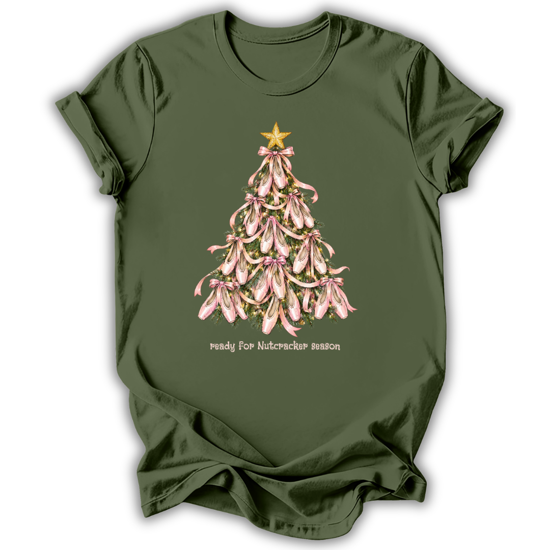 An olive green short-sleeve t-shirt with a graphic of a Christmas tree made of pink orchids with a gold star, and the text 'ready for Nutcracker season' printed below.