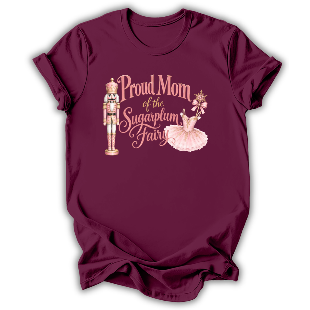 A maroon short-sleeve t-shirt with a graphic print that reads 'Proud Mom of the Sugarplum Fairy' in pink script, accompanied by illustrations of a nutcracker and a ballerina in a pink tutu, shown on a plain white background.