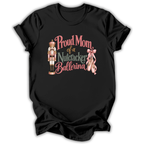A black short-sleeve t-shirt with a graphic print that reads 'Proud Mom of a Nutcracker Ballerina' in pink and green lettering, accompanied by an illustration of a nutcracker and pink ballet slippers, shown on a plain white background.
