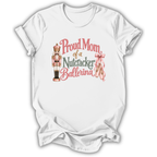 A white short-sleeve crewneck t-shirt with a graphic print that reads 'Proud Mom of a Nutcracker Ballerina' in pink and green lettering, accompanied by an illustration of a nutcracker and a pink ribbon.