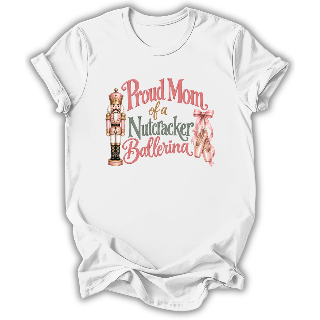 A white short-sleeve crewneck t-shirt with a graphic print that reads 'Proud Mom of a Nutcracker Ballerina' in pink and green lettering, accompanied by an illustration of a nutcracker and a pink ribbon.