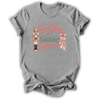 A heather gray short-sleeve t-shirt with a graphic on the front that reads 'Proud Mom of a Nutcracker Ballerina' in pink and green lettering, accompanied by an illustration of a nutcracker and a pink ribbon.
