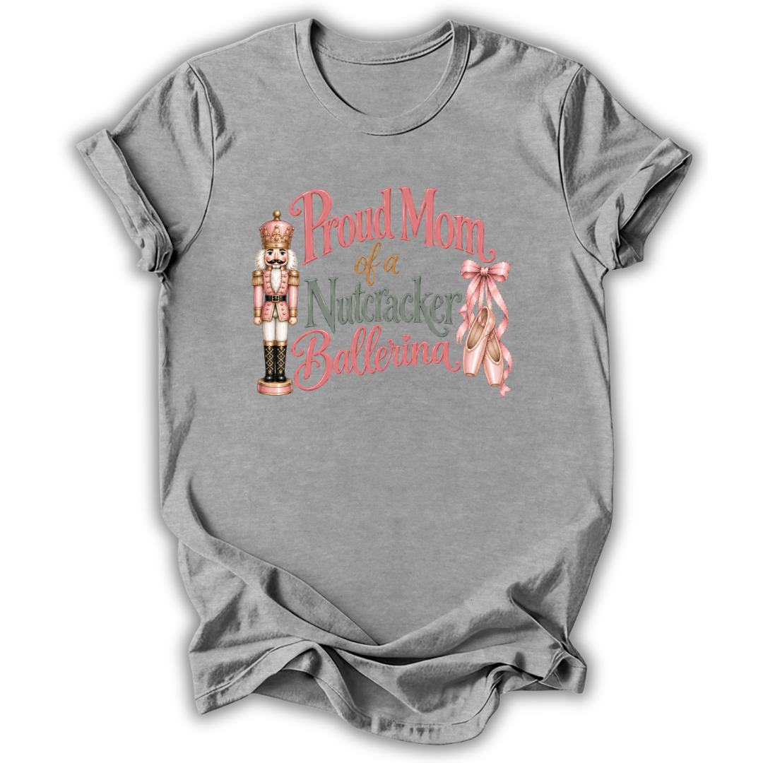 A heather gray short-sleeve t-shirt with a graphic on the front that reads 'Proud Mom of a Nutcracker Ballerina' in pink and green lettering, accompanied by an illustration of a nutcracker and a pink ribbon.