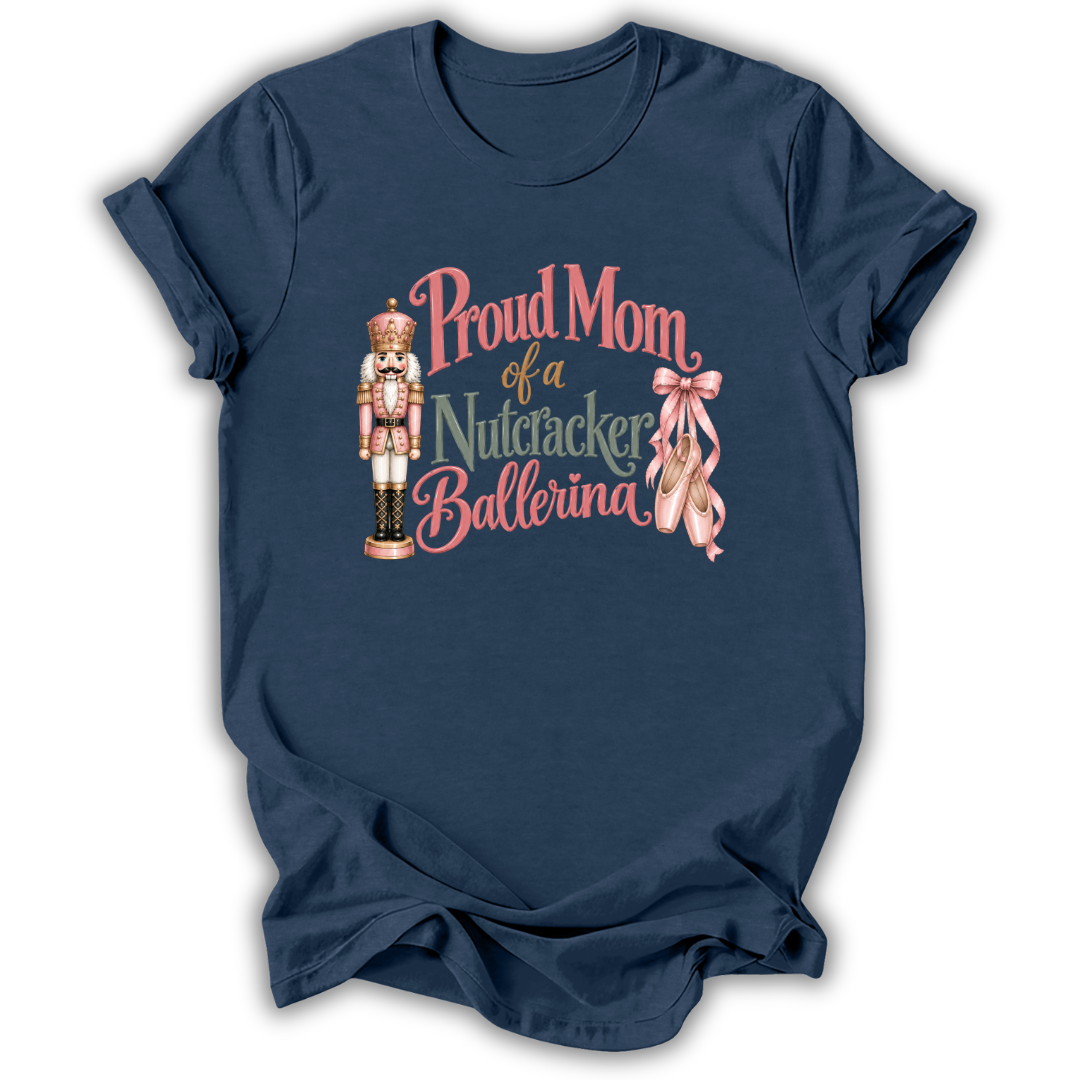 A navy blue short-sleeve t-shirt with a graphic on the front that reads 'Proud Mom of a Nutcracker Ballerina' in pink and gold lettering, accompanied by an illustration of a nutcracker and pink ballet slippers.