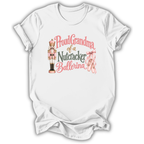 A white short-sleeve crewneck t-shirt with a graphic print on the front. The graphic features a pink and gold nutcracker, pink ballet slippers, and the text 'Proud Grandma of a Nutcracker Ballerina' in pink and gold lettering.