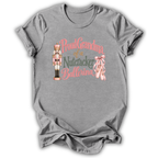 A heather gray short-sleeve t-shirt with a graphic on the front that reads 'Proud Grandma of a Nutcracker Ballerina' in pink and green lettering, accompanied by an illustration of a nutcracker and pink ballet slippers.
