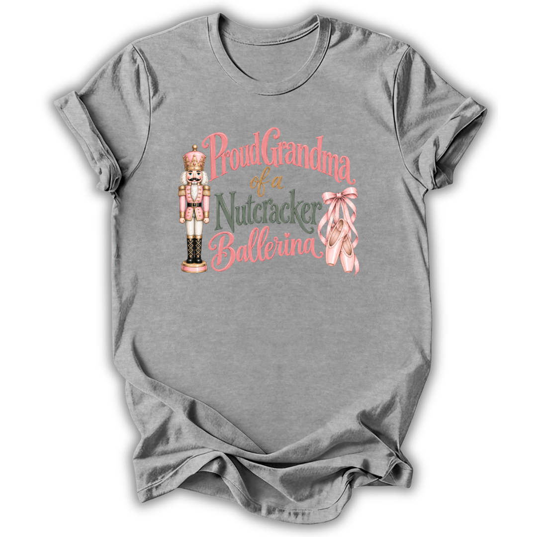 A heather gray short-sleeve t-shirt with a graphic on the front that reads 'Proud Grandma of a Nutcracker Ballerina' in pink and green lettering, accompanied by an illustration of a nutcracker and pink ballet slippers.