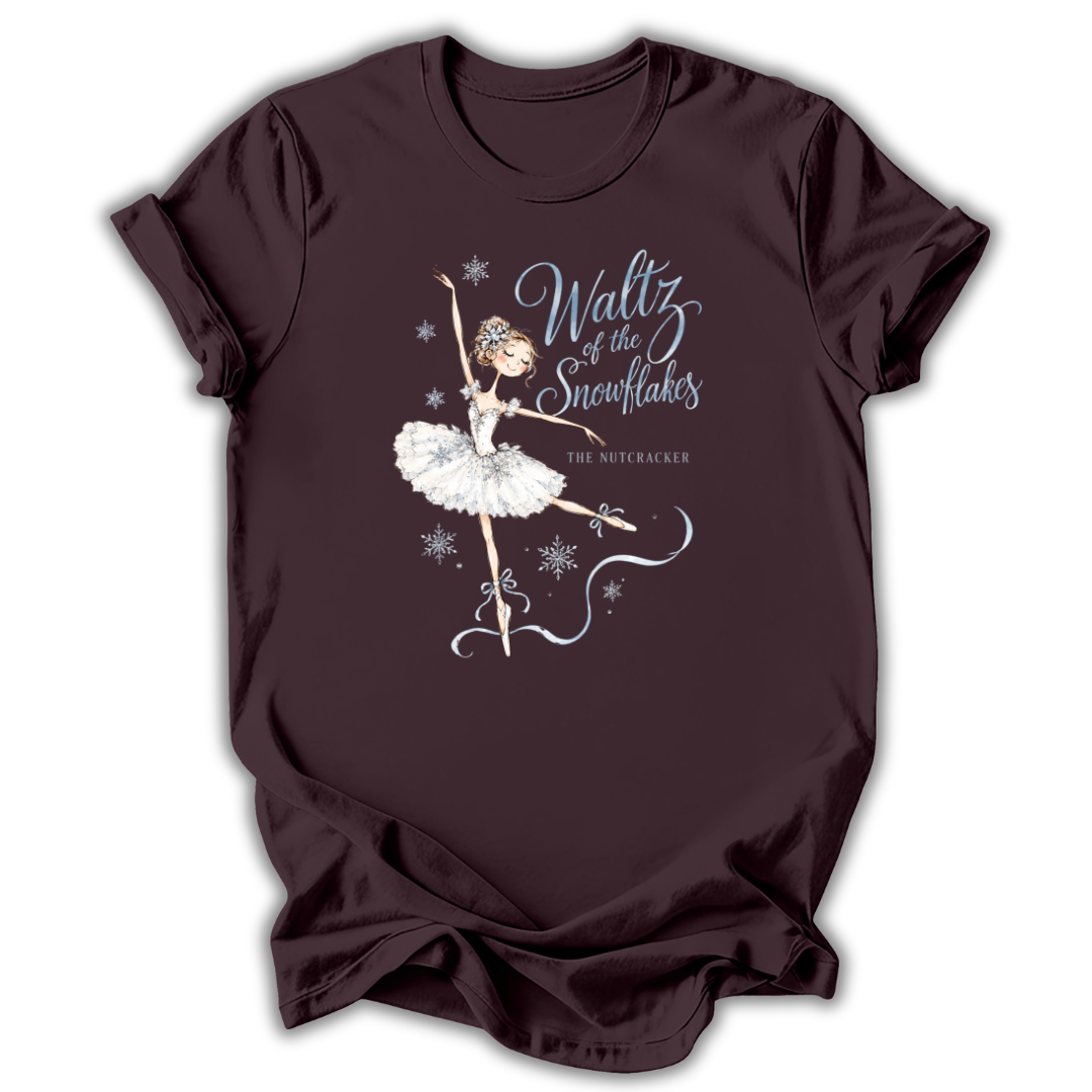 A dark brown short-sleeve t-shirt with a graphic of a ballerina in a white tutu and the text 'Waltz of the Snowflakes' and 'The Nutcracker' printed on the front, displayed against a plain white background.