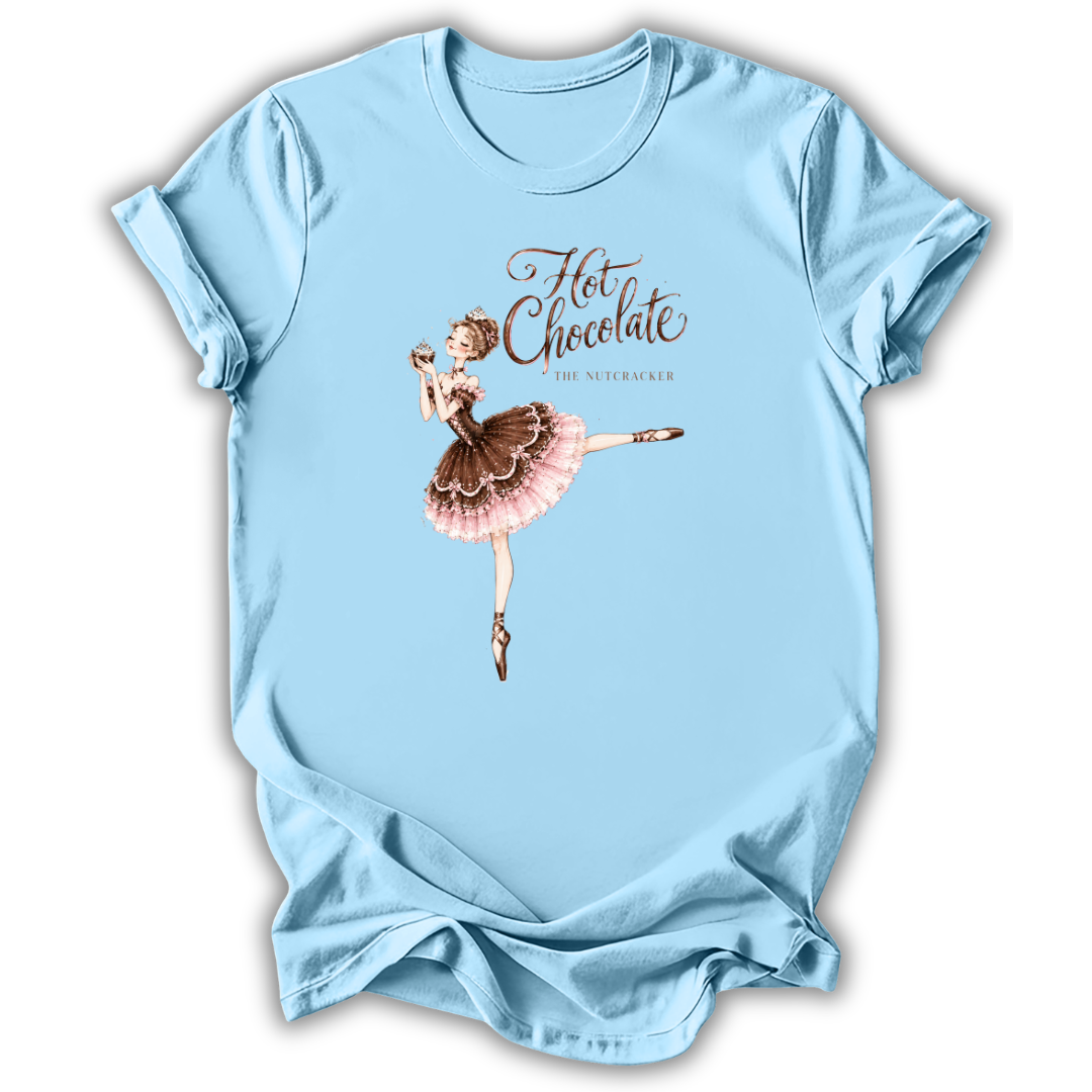 A light blue short-sleeve t-shirt with a graphic of a ballet dancer in a pink and brown tutu holding a hot chocolate cup, with the text 'Hot Chocolate' and 'the nutmaker' printed on the front.