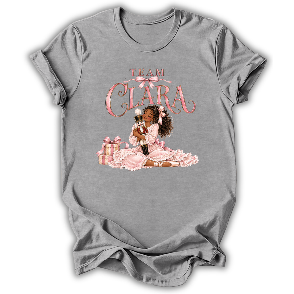 A gray short-sleeve crewneck t-shirt with a custom graphic print. The graphic features the text 'TEAM CLARA' in pink glitter-style lettering above an illustration of a Black woman in a pink dress holding a cat, with pink gift boxes.