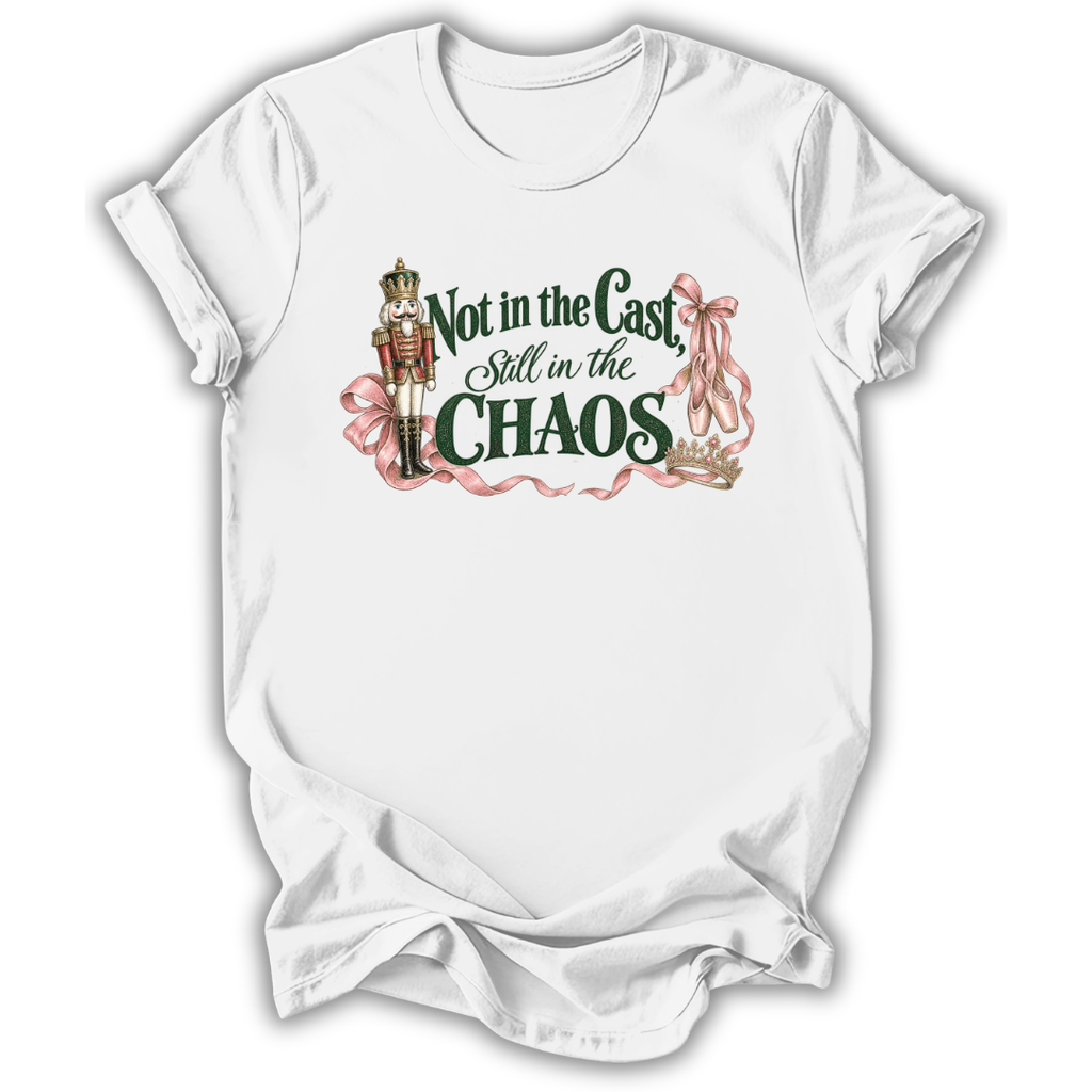 A white short-sleeve t-shirt with a graphic print on the front. The graphic features a nutcracker soldier, pink ribbons, and the text 'Not in the Cast, Still in the CHAOS' in dark green and pink lettering.