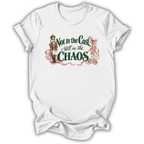 A white short-sleeve t-shirt with a graphic print on the front. The graphic features a nutcracker soldier, pink ribbons, and the text 'Not in the Cast, Still in the CHAOS' in dark green and pink lettering.