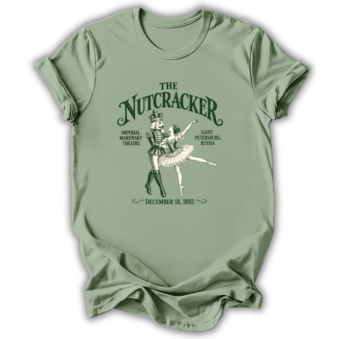 A sage green short-sleeve t-shirt with a vintage-style graphic of 'The Nutcracker' ballet, featuring a nutcracker soldier and ballerina with text detailing the Saint Petersburg premiere on December 18, 1892.