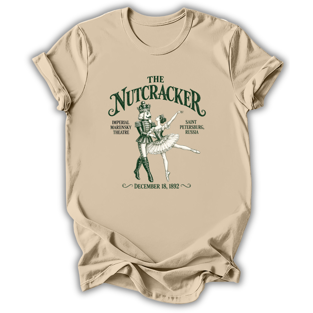 A beige short-sleeve t-shirt with a vintage-style green graphic of The Nutcracker ballet, featuring the title and historical performance details, displayed on a clean white background.