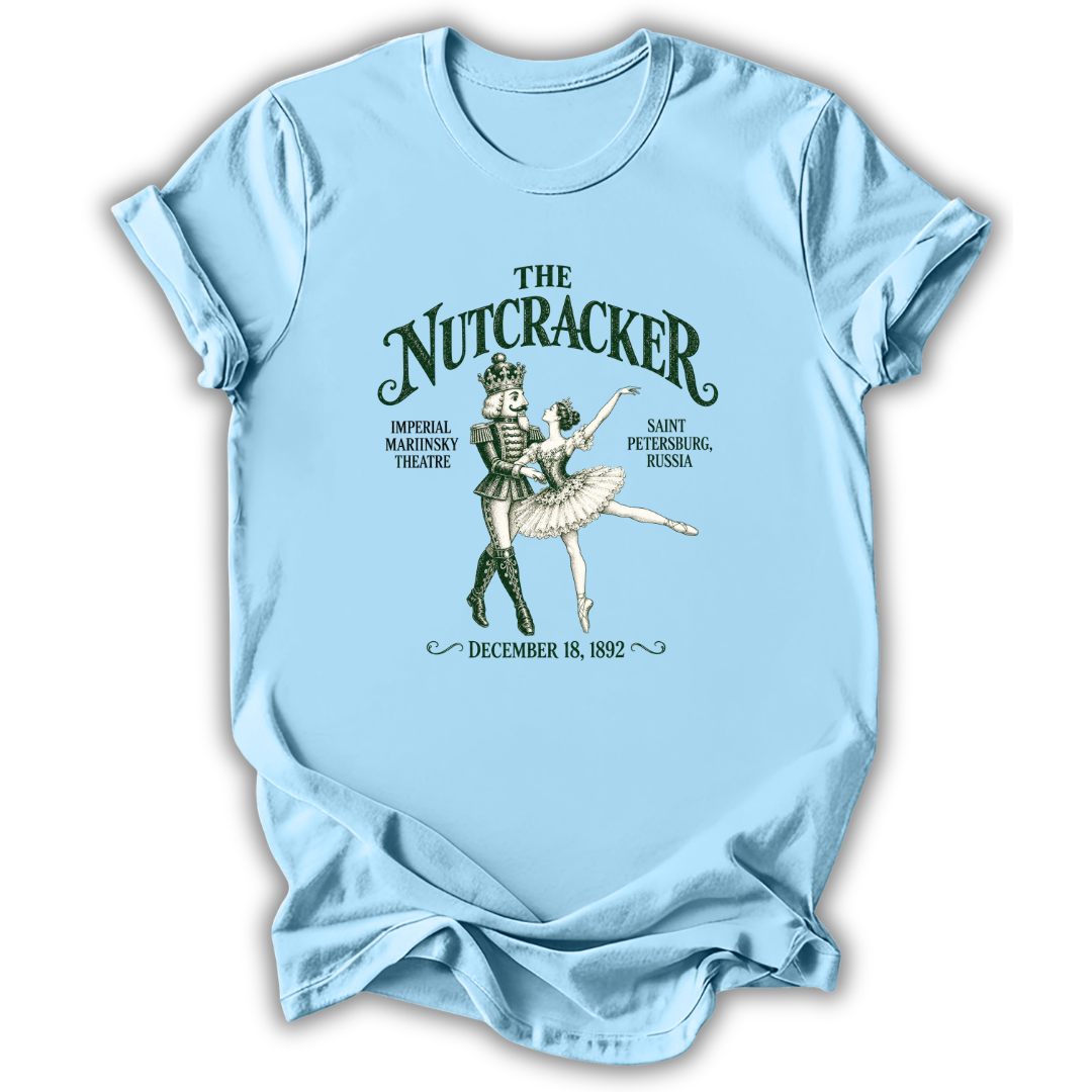 A light blue short-sleeve t-shirt with a vintage-style graphic of 'The Nutcracker' ballet, featuring a nutcracker and ballerina illustration with text details, displayed on a clean white background.