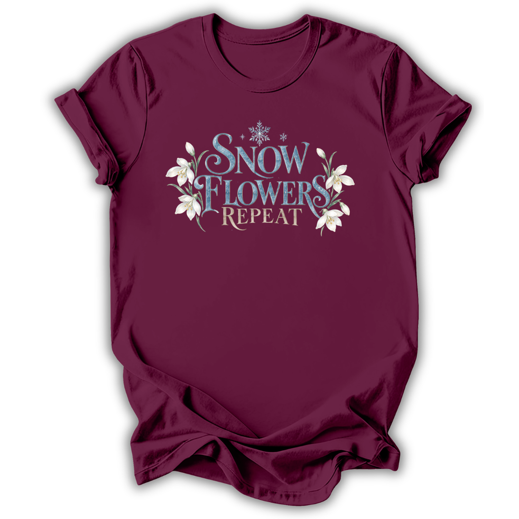 A maroon short-sleeve t-shirt with a graphic on the chest that reads 'SNOW FLOWERS REPEAT' in blue and gold lettering, decorated with white snowflakes and flowers, shown on a white background.