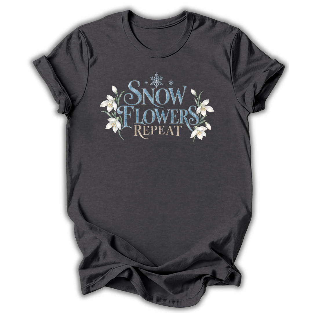 Dark gray short-sleeve t-shirt with a graphic on the chest that reads 'SNOW FLOWERS REPEAT' in blue and gold lettering, decorated with white snowflakes and flowers, shown on a white background.