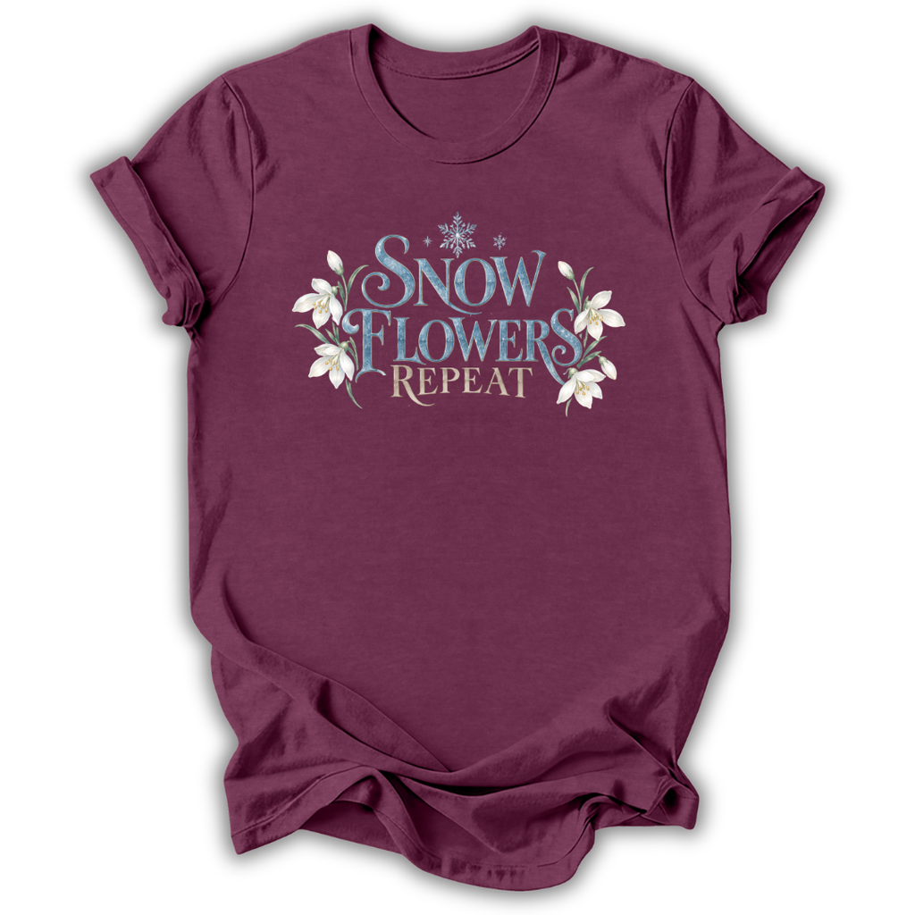 Heather maroon short-sleeve t-shirt with a graphic on the chest that reads 'SNOW FLOWERS REPEAT' in blue and gold lettering, decorated with white snowflakes and flowers, shown on a white background.