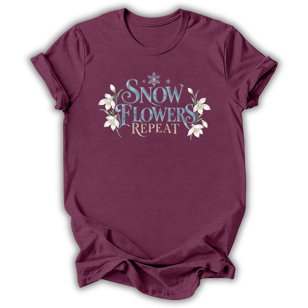 Heather maroon short-sleeve t-shirt with a graphic on the chest that reads 'SNOW FLOWERS REPEAT' in blue and gold lettering, decorated with white snowflakes and flowers, shown on a white background.